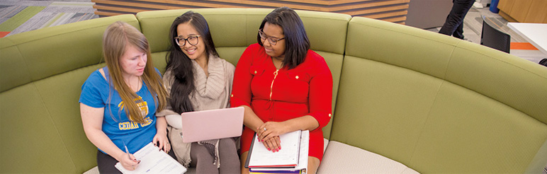 A group of female students relax & work on campus