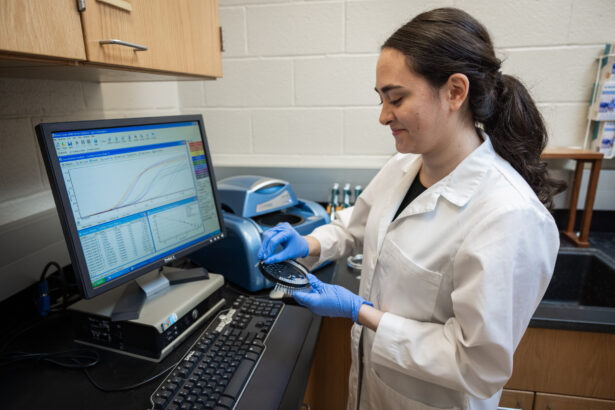 Forensic science student stands in front of the computer, pulling strands off a hairbrush to analyze